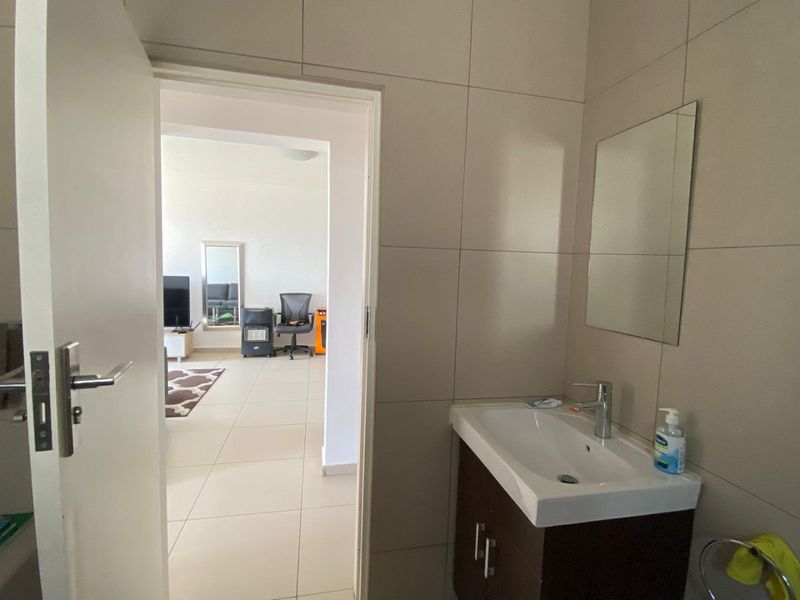 A compact bathroom featuring a modern vanity cabinet with a ceramic basin and chrome mixer tap, complemented by neutral wall tiling.