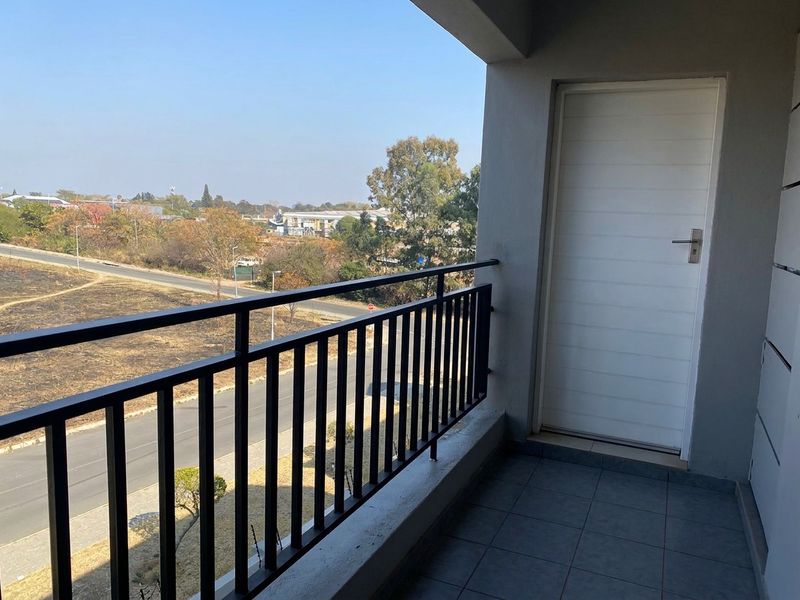A clean, covered balcony featuring tiled flooring and a metal balustrade, offering an open view of the surrounding area.