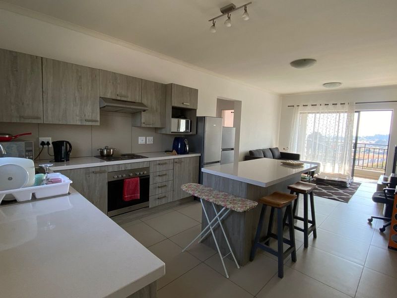 An open-plan kitchen and living area featuring modern grey cabinetry, stone countertops, a central island, and direct access to a balcony through sliding doors.