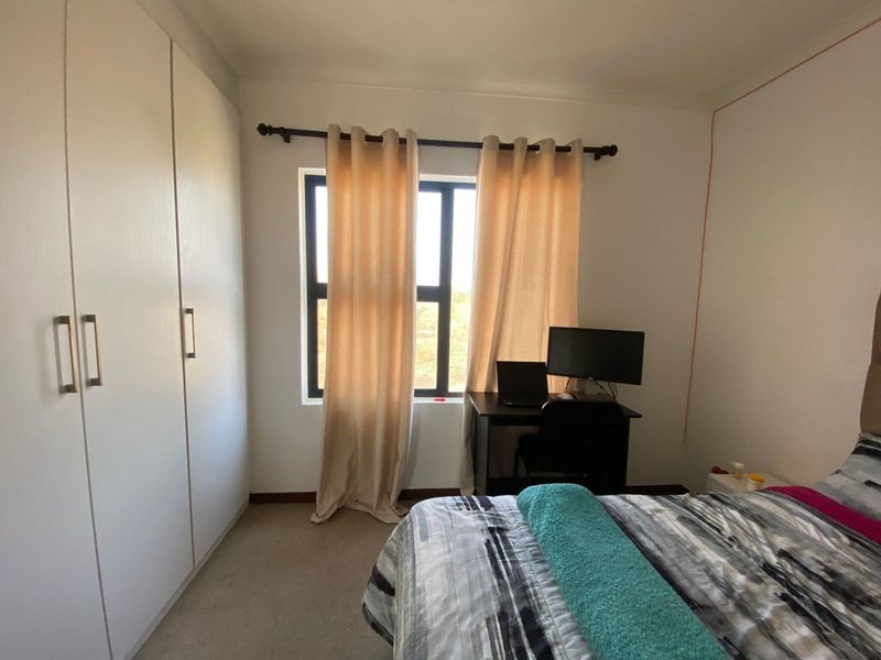 A functional bedroom featuring built-in cupboards and an aluminium-framed window, providing natural light and storage space.