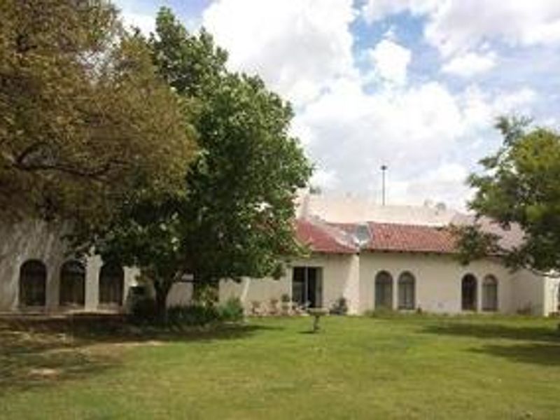 Rear view of the farm property featuring a stucco facade, arched windows, a tiled roof, and a spacious garden area.