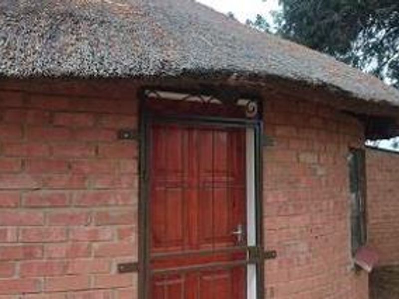 Exterior view of a traditional round farm building featuring exposed brick walls, a thatched roof, and a secure timber entrance door.
