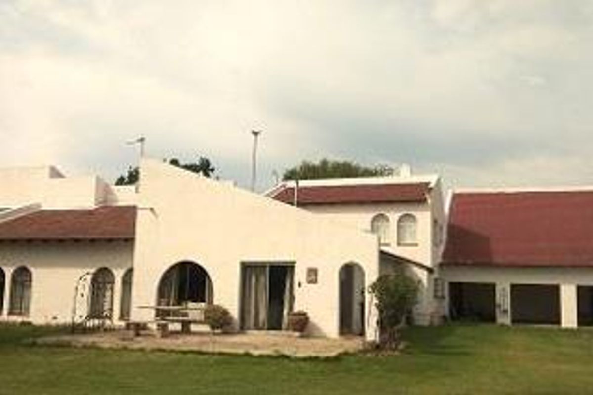 Rear view of a farm-style residence featuring a paved patio, arched architectural details, and integrated garage access set against a lawn.