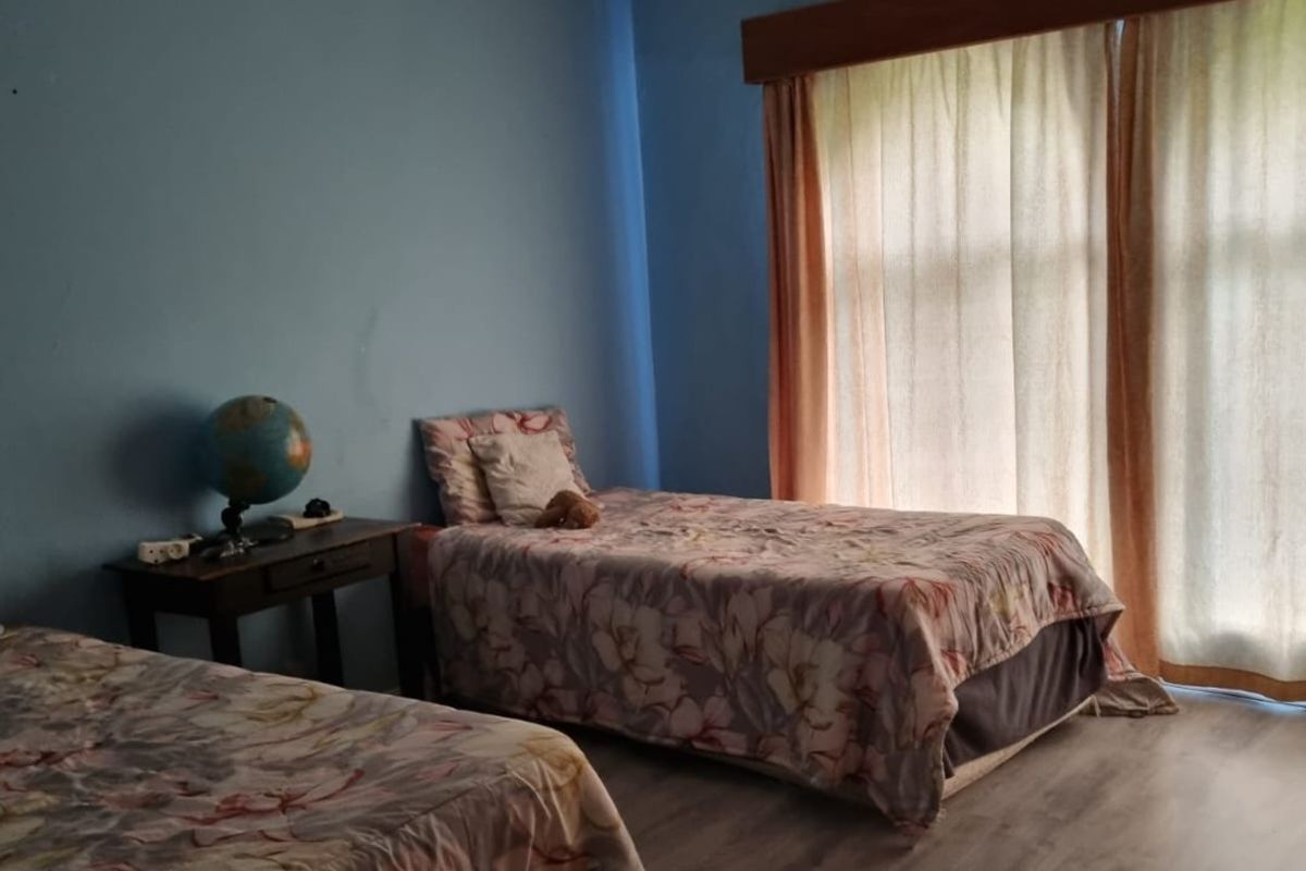 A bedroom featuring laminate flooring, a ceiling fan, and large windows with curtain rails, providing a functional space with natural light.