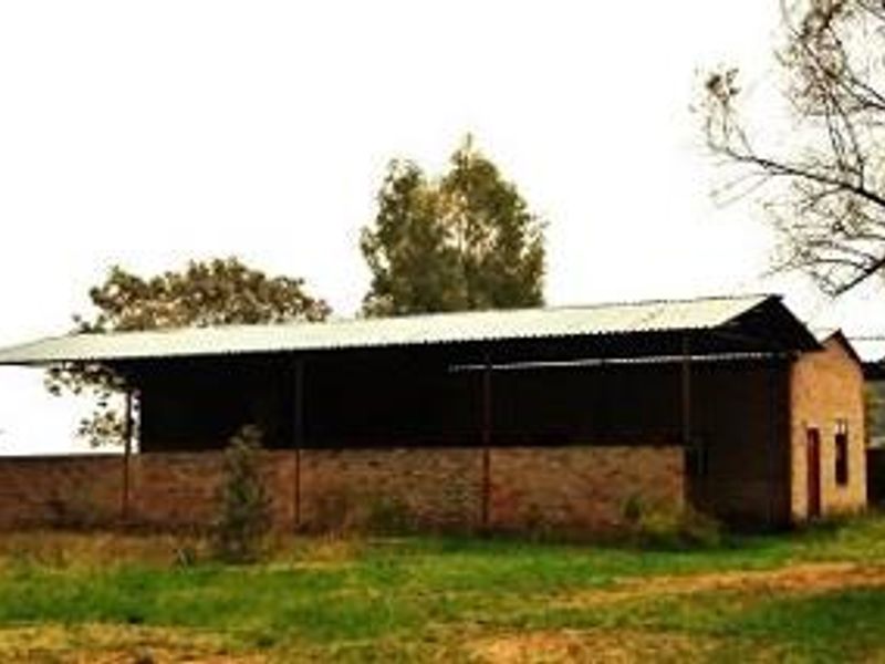 An open-sided farm structure featuring brick masonry walls and a corrugated metal roof, set within a rural landscape.