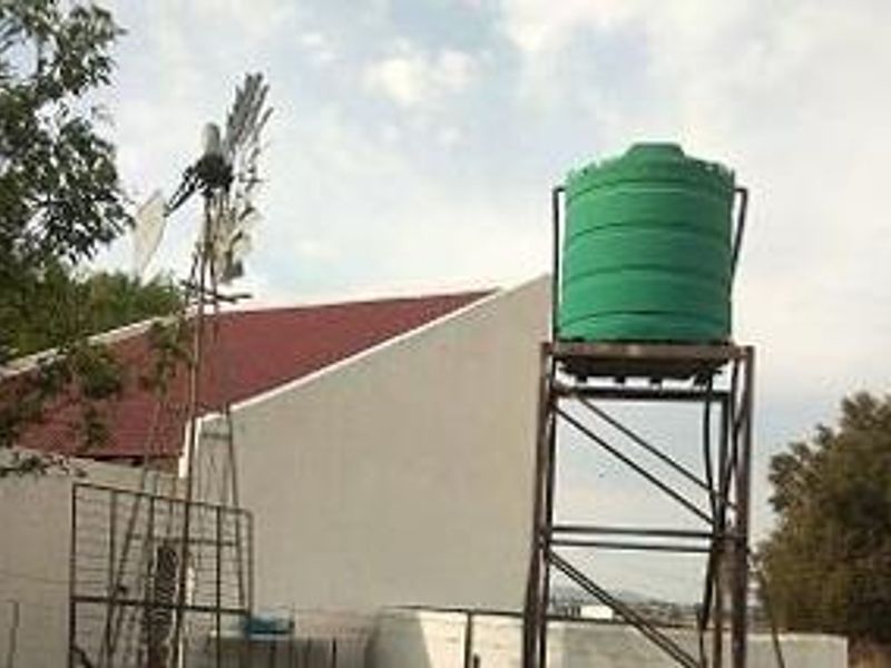 Exterior view of a farm property featuring a traditional windmill and a raised water storage tank with a metal support structure.