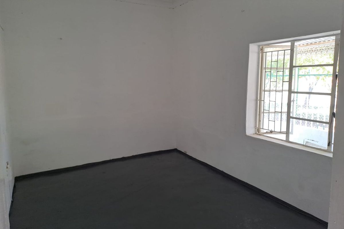 An empty bedroom featuring painted concrete flooring and a window fitted with security bars.