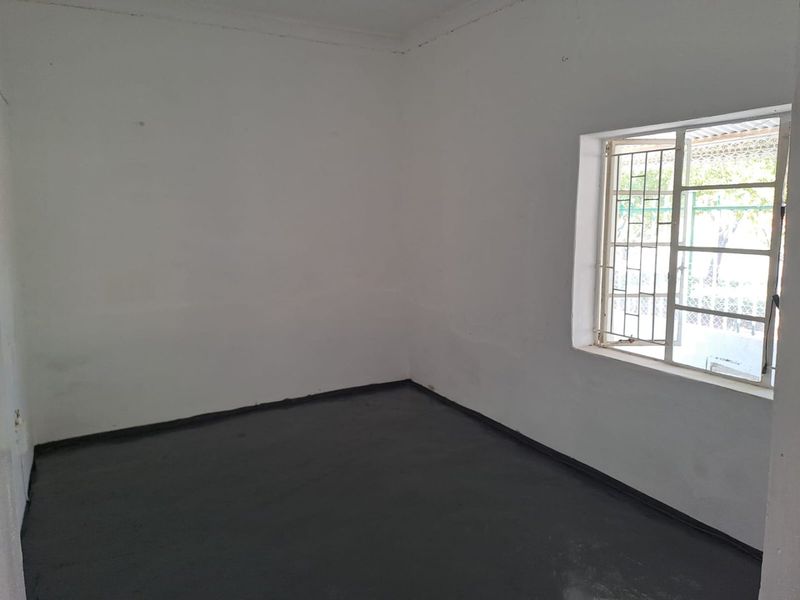 An empty bedroom featuring painted concrete flooring and a window fitted with security bars.