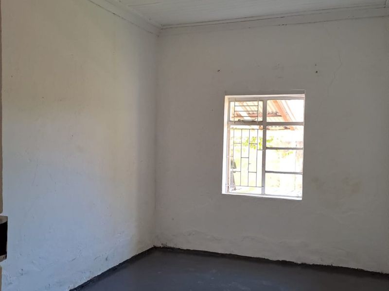 An empty bedroom featuring a painted concrete floor, timber ceiling, and a window fitted with security bars.