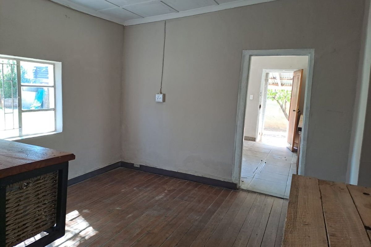 An empty living area featuring original timber flooring, a tiled ceiling, and a view through to an adjacent room.