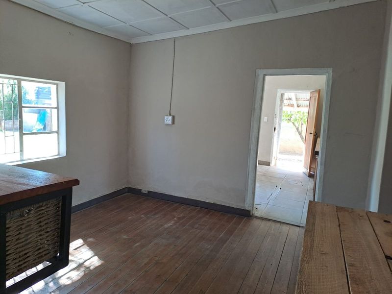 An empty living area featuring original timber flooring, a tiled ceiling, and a view through to an adjacent room.