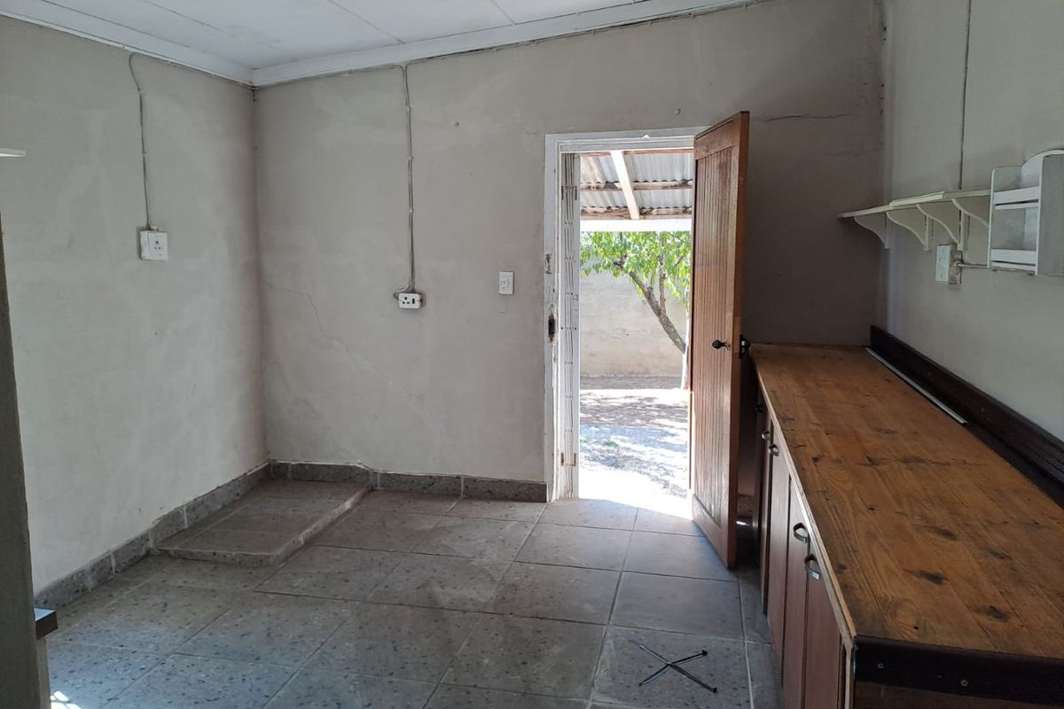 A basic, empty kitchen area featuring tiled flooring, wooden cabinetry, and direct access to the rear exterior.