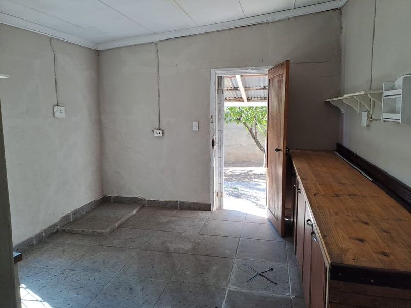 A basic, empty kitchen area featuring tiled flooring, wooden cabinetry, and direct access to the rear exterior.