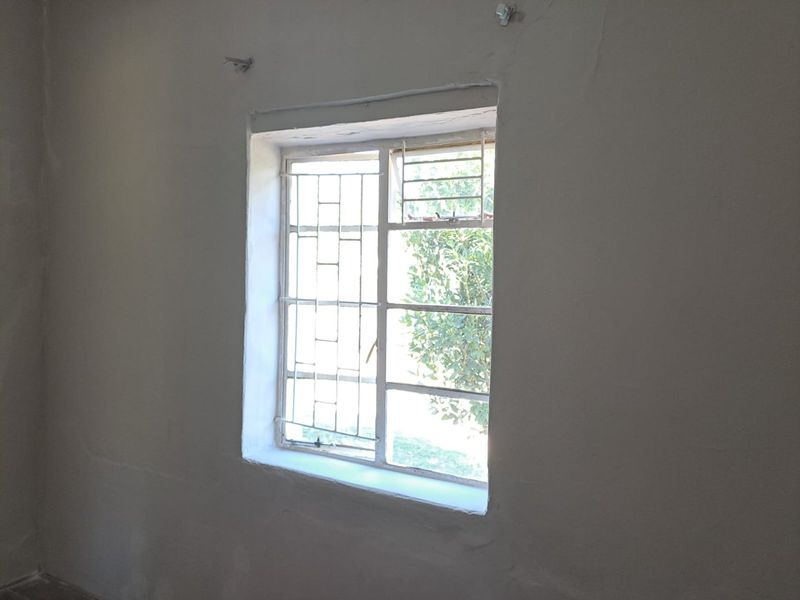 An empty room featuring a window with integrated metal security bars and unfinished wall plastering.