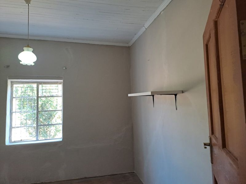 An empty bedroom featuring a timber ceiling, steel window with security bars, and a wall-mounted shelf, requiring cosmetic updates to the wall finishes.