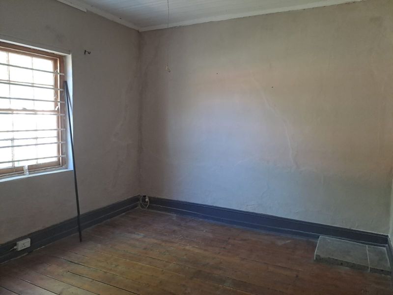 An empty bedroom featuring original timber flooring, security bars on the window, and walls requiring cosmetic attention.