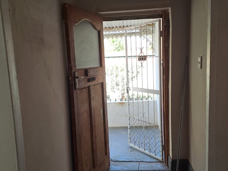 An entry hallway featuring timber flooring and a security gate leading to an outdoor area, showing signs of wear and requiring cosmetic updates.
