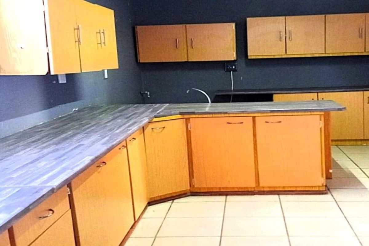 A dated kitchen featuring wood-tone cabinetry, dark laminate countertops, and tiled flooring, offering a blank canvas for potential modernization and renovation.