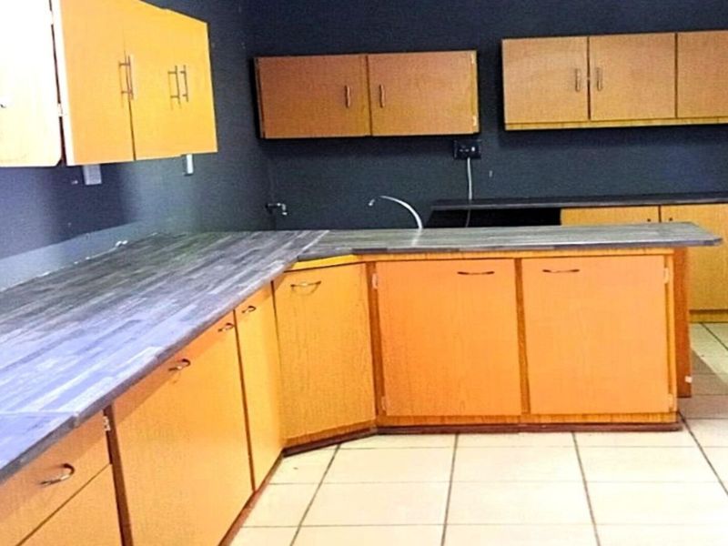A dated kitchen featuring wood-tone cabinetry, dark laminate countertops, and tiled flooring, offering a blank canvas for potential modernization and renovation.