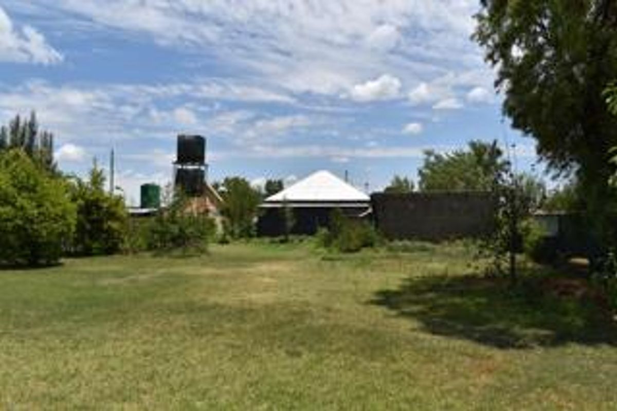 A view of the rear garden area featuring a large lawn, mature trees, and visible water storage tanks against the property structure.