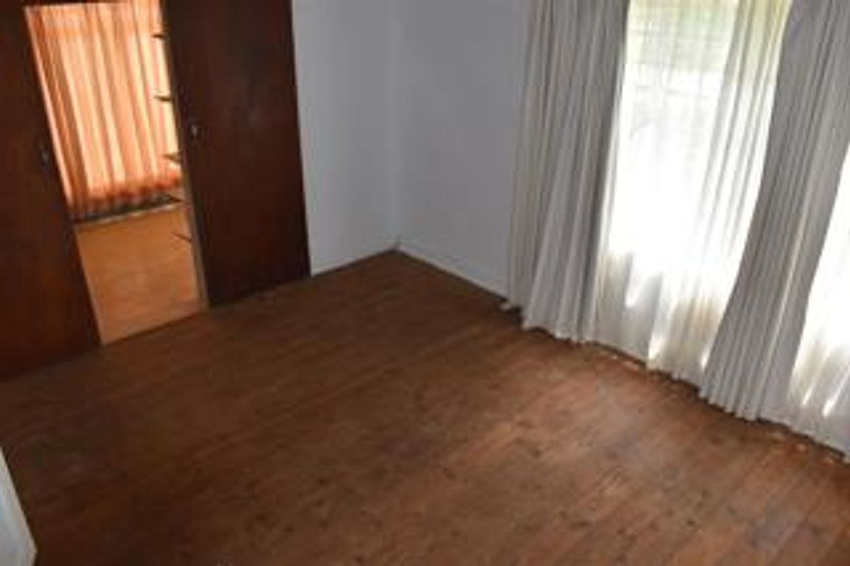 An empty bedroom featuring original timber flooring and a built-in wooden wardrobe, offering a blank canvas for renovation.
