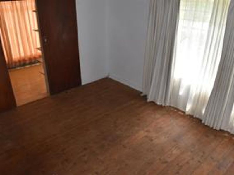 An empty bedroom featuring original timber flooring and a built-in wooden wardrobe, offering a blank canvas for renovation.