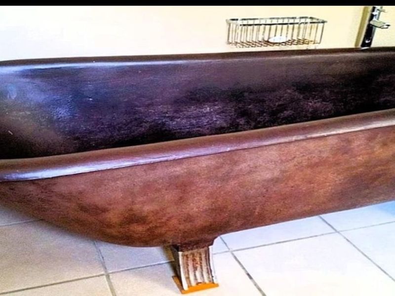 A bathroom featuring a vintage-style freestanding bathtub with a worn finish, set against tiled flooring and a wall-mounted wire storage rack.