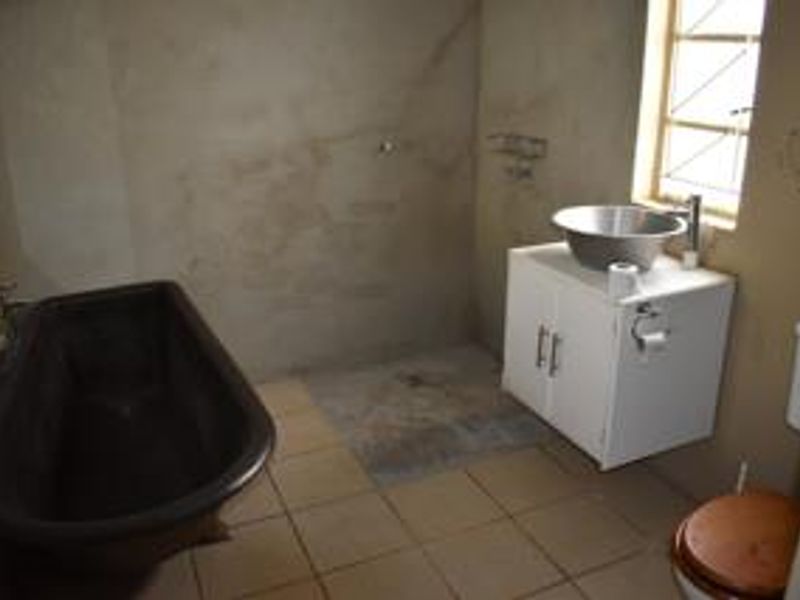 A bathroom featuring a freestanding bathtub, vanity with vessel sink, and toilet, currently requiring wall finishing and cosmetic updates.