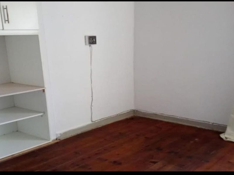 An empty bedroom featuring timber flooring and built-in shelving units, requiring minor cosmetic updates to the flooring and wall finishes.