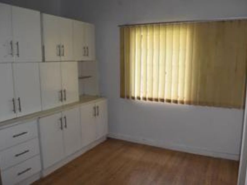 A clean, empty bedroom featuring white built-in cabinetry, laminate flooring, and vertical window blinds.