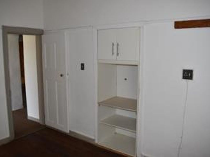 An empty bedroom featuring timber flooring, a built-in cupboard, and a doorway leading to an adjacent room.