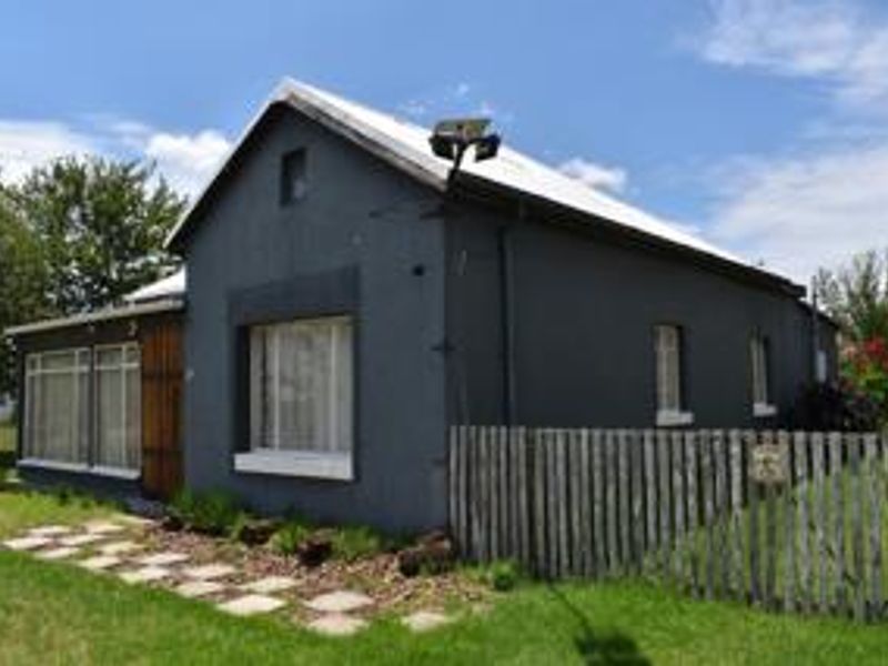 A detached house featuring a dark grey exterior, metal roofing, and a timber fence, set within a grassy yard with a paved walkway.