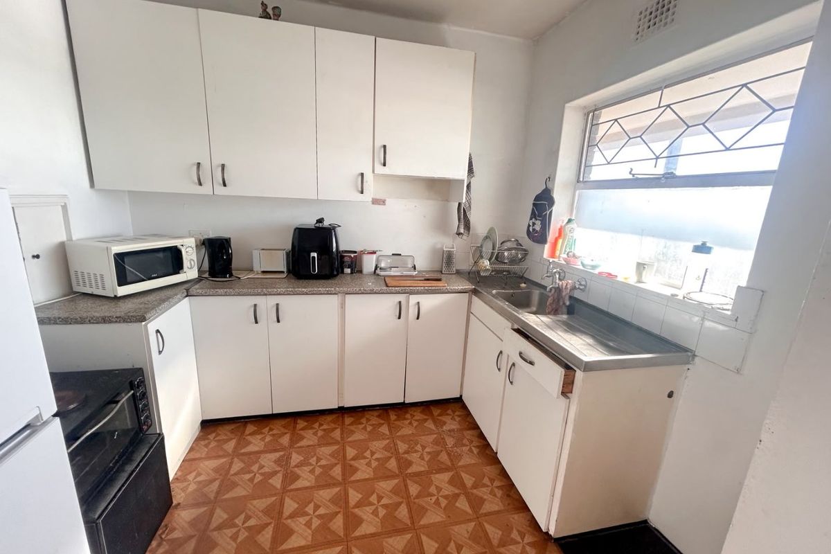 A functional kitchen featuring white cabinetry, laminate countertops, a stainless steel sink, and patterned tiled flooring, offering potential for modernization.