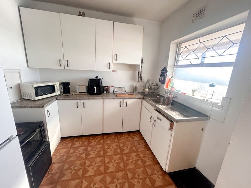 A functional kitchen featuring white cabinetry, laminate countertops, a stainless steel sink, and patterned tiled flooring, offering potential for modernization.