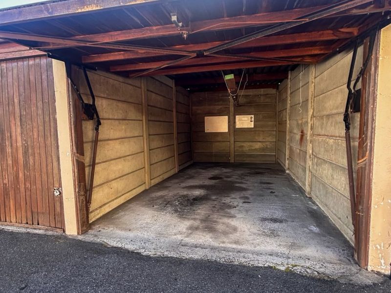 A single-car garage featuring concrete panel walls, an exposed timber roof structure, and a manual up-and-over door.