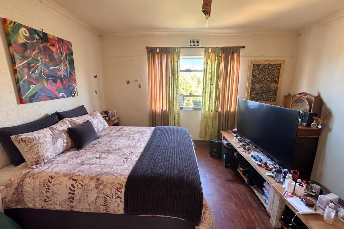 A bedroom featuring parquet flooring, a ventilation grille, and cornice detailing, offering a functional space with potential for cosmetic updates.