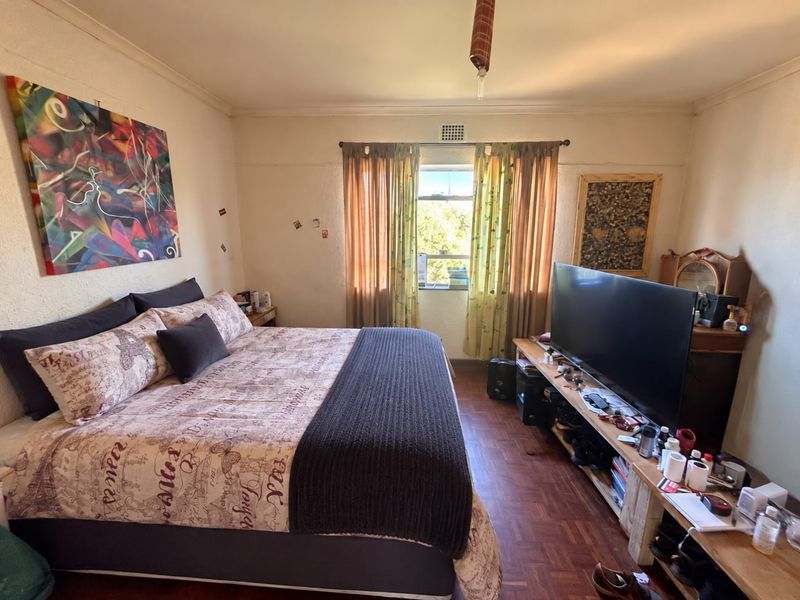 A bedroom featuring parquet flooring, a ventilation grille, and cornice detailing, offering a functional space with potential for cosmetic updates.