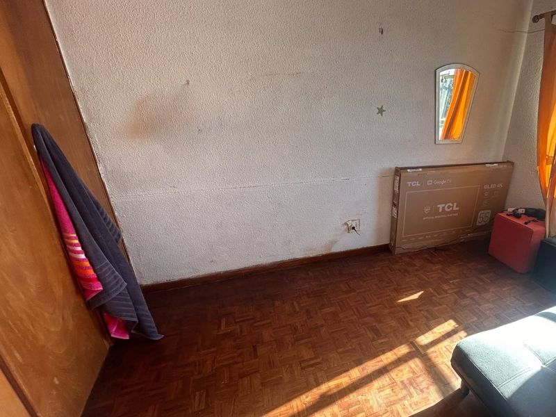 A bedroom featuring original parquet flooring and a built-in wardrobe, requiring cosmetic updates to the wall finishes and general maintenance.