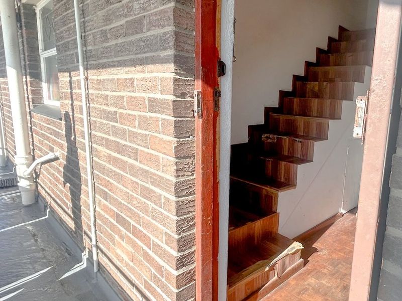 Entrance area featuring a brick facade and an internal wooden staircase with parquet flooring, showing signs of wear and requiring maintenance.