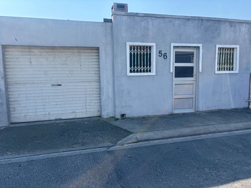 Front elevation of a residential property featuring a roller garage door, security-barred windows, and a street-facing entrance.