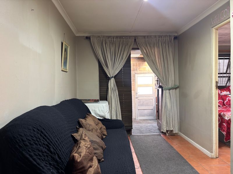 A living room featuring tiled flooring and direct access to an outdoor area, showing signs of wear on the walls.