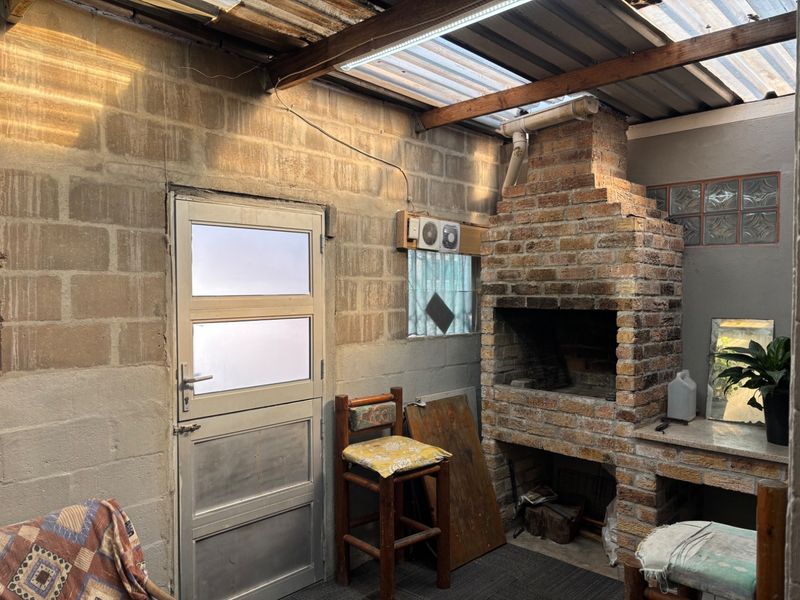 Covered outdoor patio area featuring a built-in brick braai, exposed block walls, and a translucent roof, offering a rustic space for outdoor entertaining.