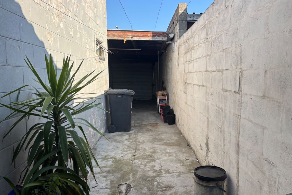 A narrow exterior side passage featuring concrete paving and cinder block boundary walls leading to a garage entrance.