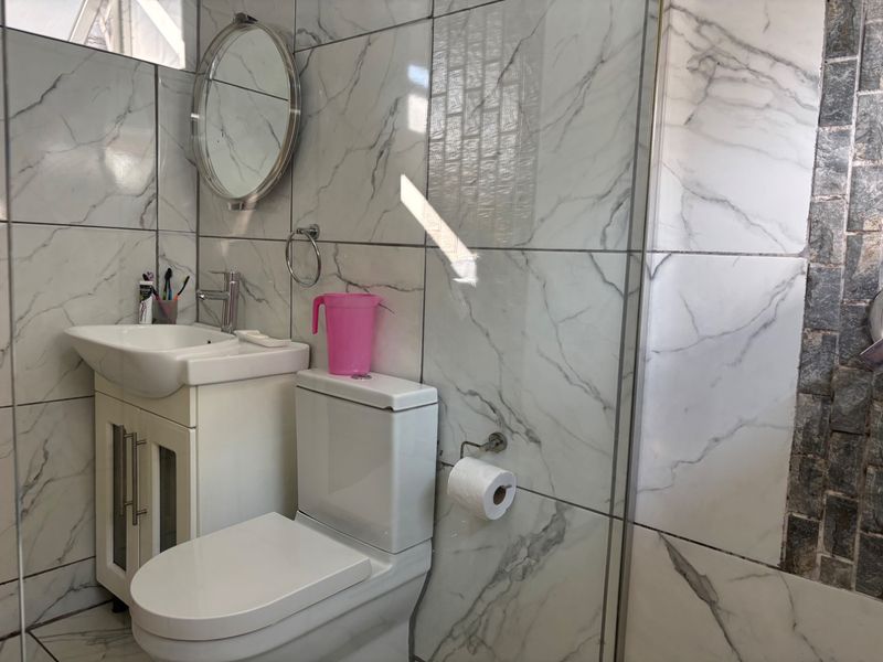 A modern bathroom featuring marble-look wall tiles, a vanity cabinet with a basin, a toilet, and a glass shower screen.