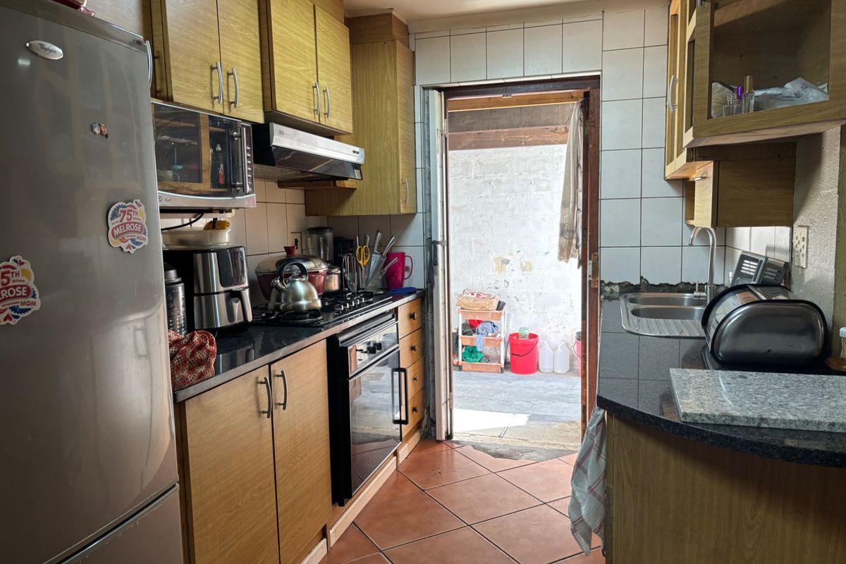 A functional kitchen featuring wooden cabinetry, granite countertops, built-in oven, gas hob, and direct access to an outdoor area.