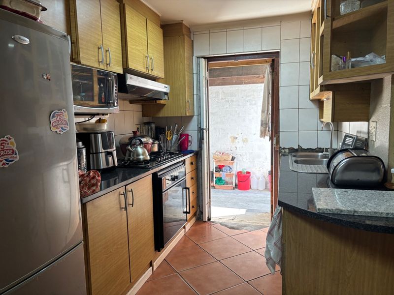 A functional kitchen featuring wooden cabinetry, granite countertops, built-in oven, gas hob, and direct access to an outdoor area.