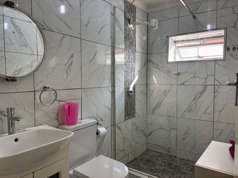 Modern bathroom featuring marble-look wall tiles, a glass-enclosed shower with mosaic flooring, a vanity basin, and a toilet.