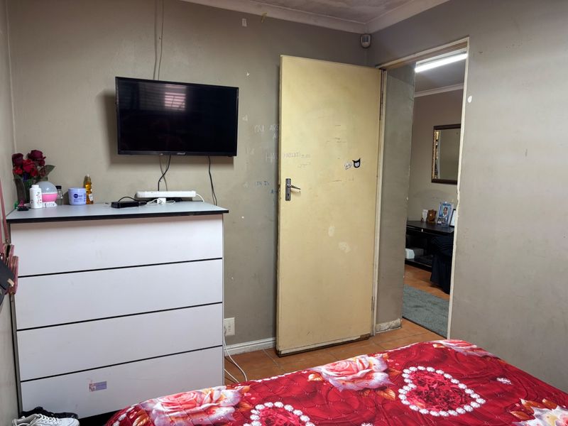 A bedroom featuring tiled flooring and a standard internal door, showing signs of wear on the walls and door surface.