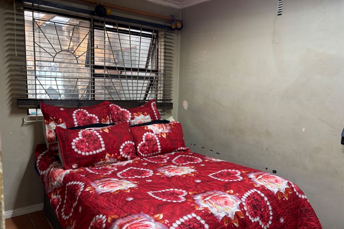 A bedroom featuring tiled flooring, security bars on the window, and venetian blinds, requiring cosmetic wall repairs and fresh paint.