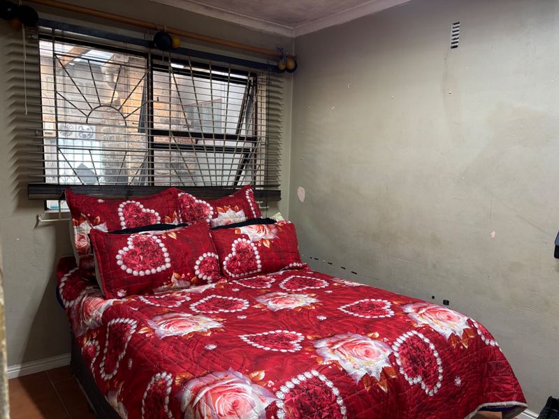 A bedroom featuring tiled flooring, security bars on the window, and venetian blinds, requiring cosmetic wall repairs and fresh paint.